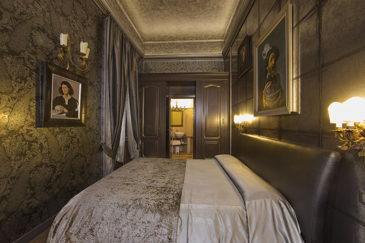 Una habitación con una cama grande, un candelabro y retratos enmarcados en las paredes.