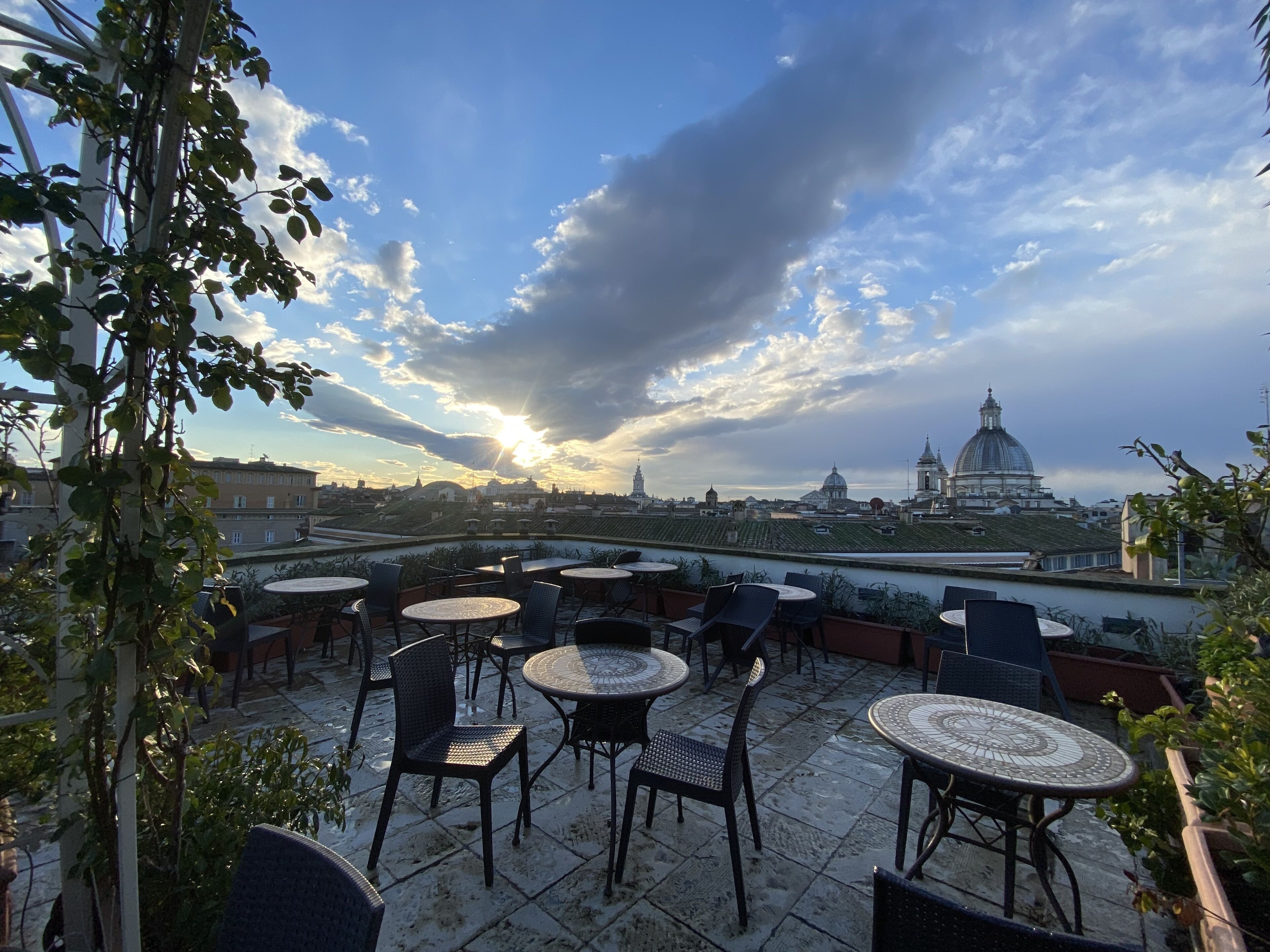 Une terrasse sur le toit, dotée de tables et de chaises rondes, offrant une vue sur le paysage urbain, avec ses bâtiments historiques et sa structure en forme de dôme.