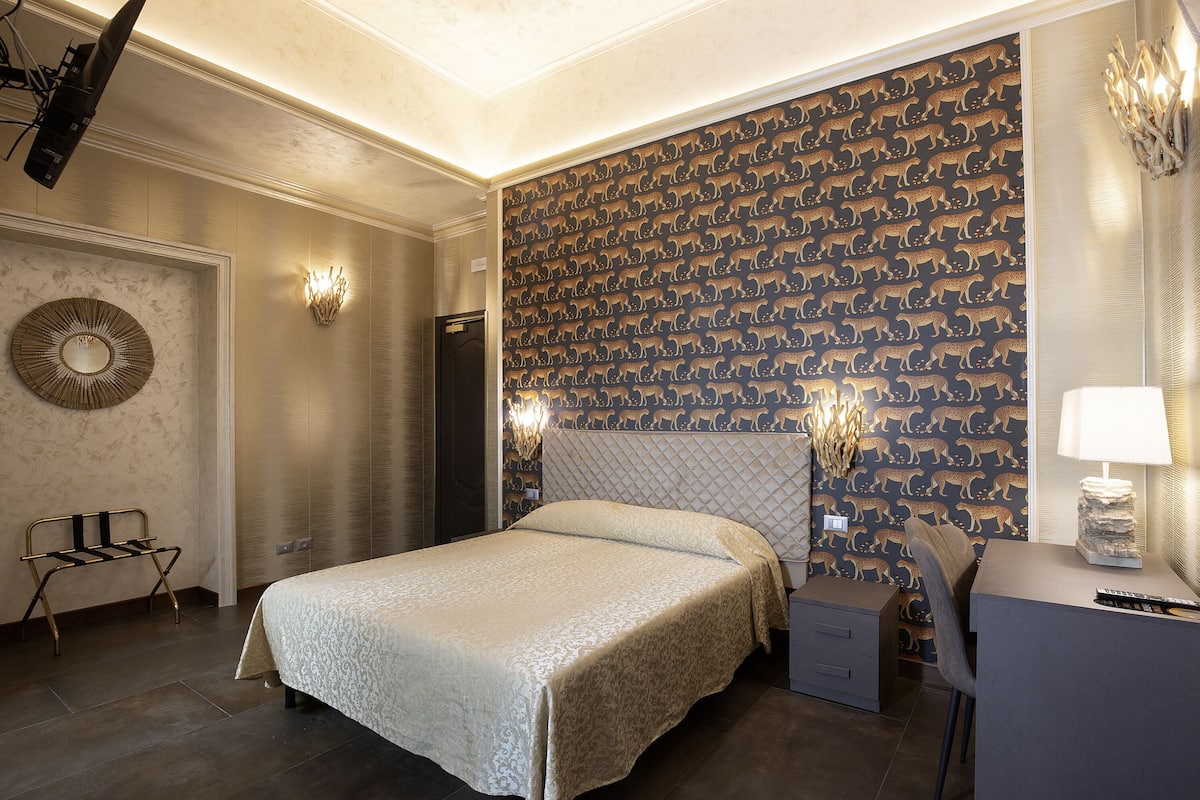 Habitación de hotel con una cama grande, un escritorio con lámpara y un papel tapiz estampado.