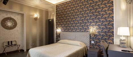 A hotel room with a large bed, a desk with a lamp, and a patterned wallpaper.