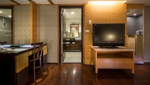 A modern hotel room with a wooden floor, a desk with a chair, a television on a wooden stand, and a bathroom visible through an open door. - Waikoloa Hotel (Taipei)