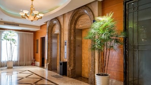 A hotel lobby with a marble floor, a large potted plant, and three elevators. - Waikoloa Hotel (Taipei)