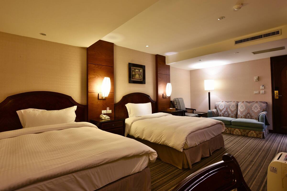 A hotel room with two beds, a sofa, a desk, and a chair.