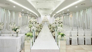 A long aisle with white floral arrangements and chairs on both sides, leading to a central area with a chandelier. - Koryo Hotel (Bucheon)