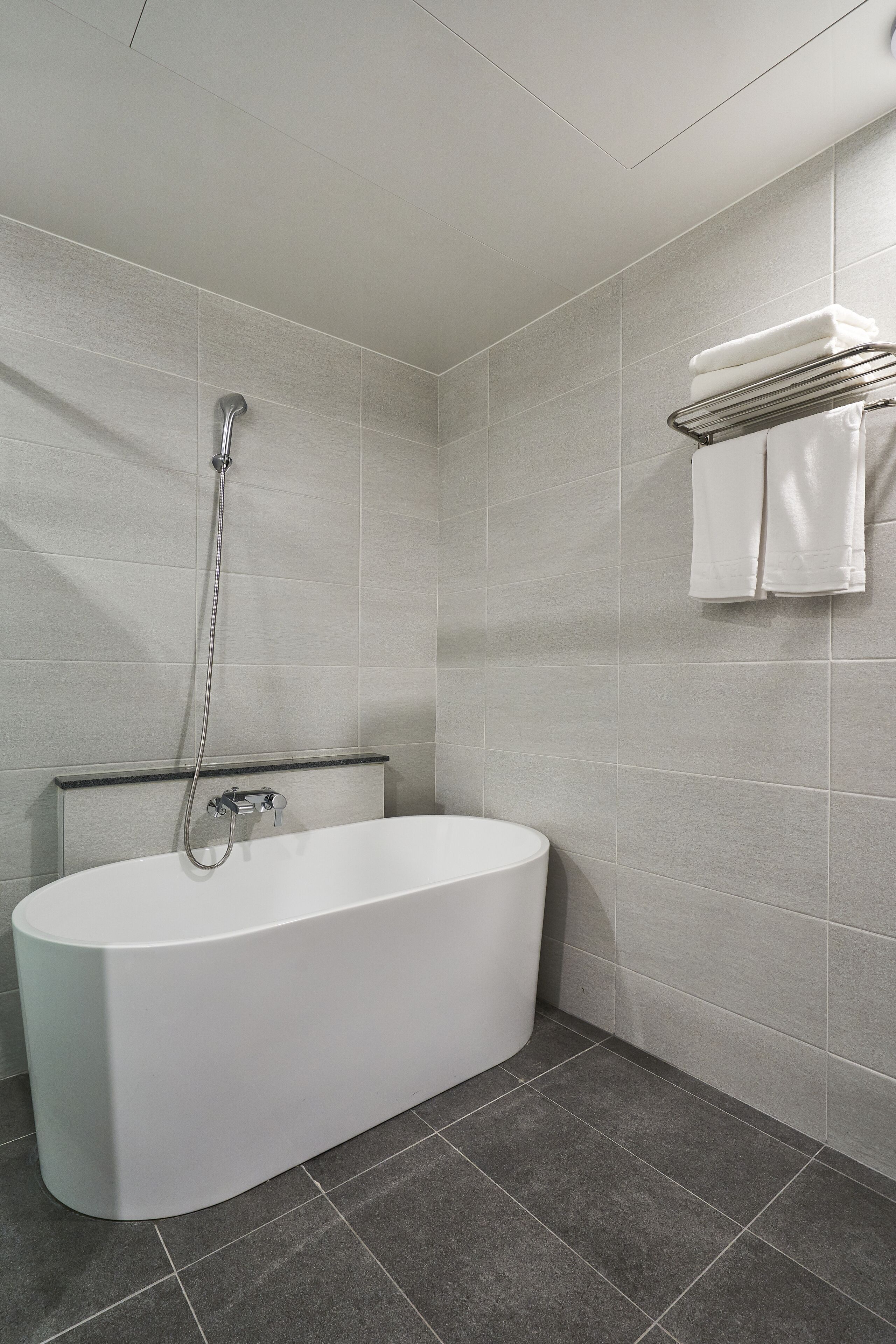 Un baño moderno con una bañera independiente, un perchero con toallas dobladas y un cabezal de ducha.