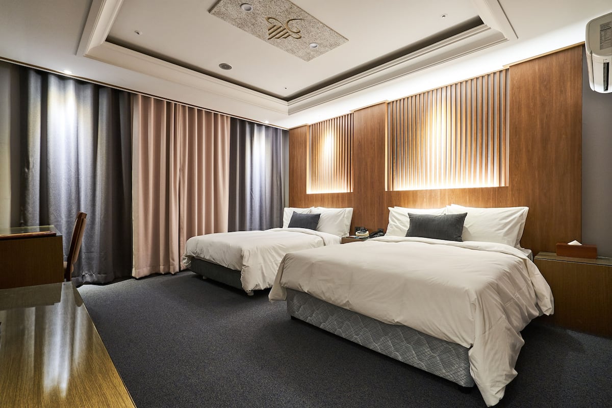 Habitación de hotel con dos camas, un escritorio y un ventanal grande con cortinas.