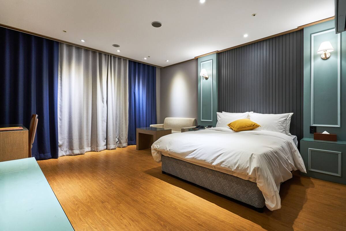 Una habitación de hotel moderna con una cama grande, una mesita de noche, una silla y un escritorio.