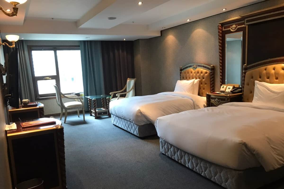 Habitación de hotel con dos camas, un escritorio, una silla, una mesita y un espejo grande.