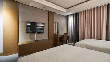 A hotel room with two beds, a desk, a chair, a TV, and a large window with curtains.