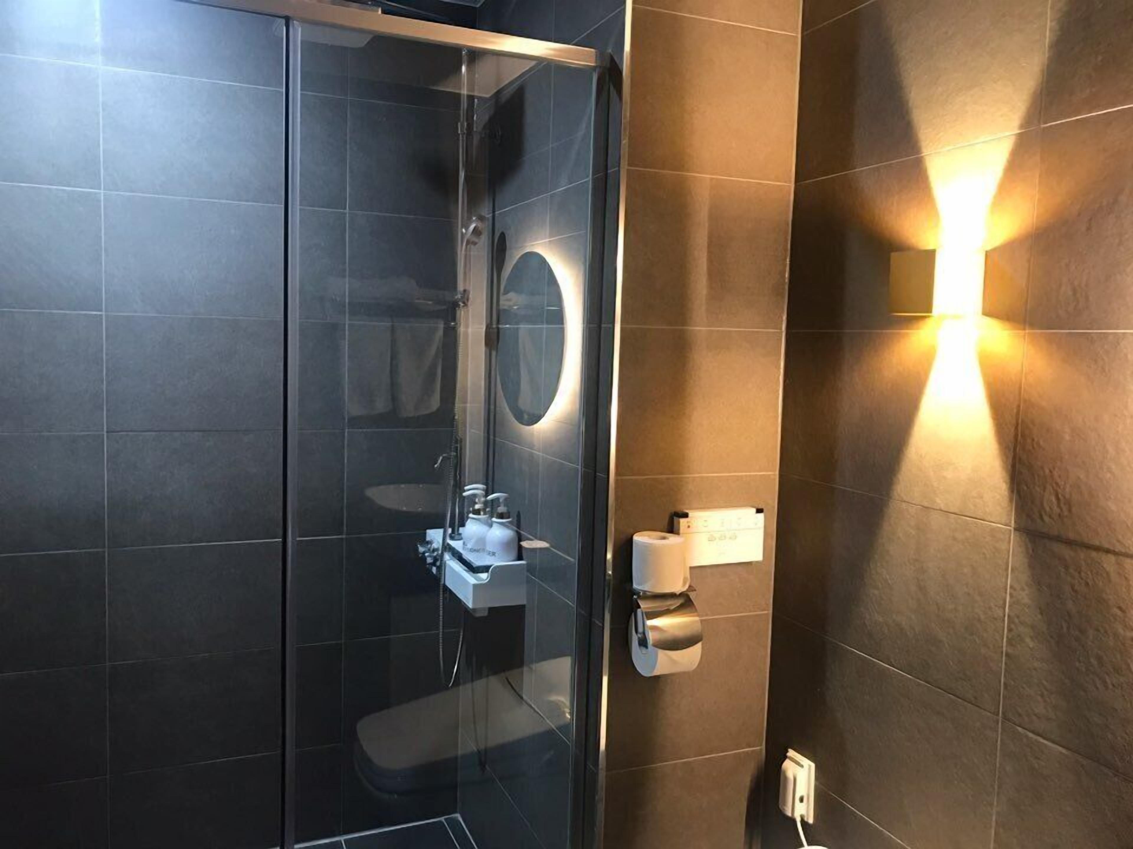 A modern bathroom with a glass-enclosed shower, a white sink, and a wall-mounted toilet paper dispenser.
