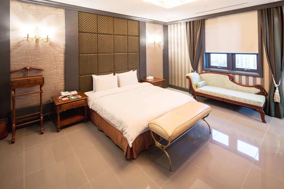 Una habitación de hotel con una cama grande, una mesita de noche, un aparador de madera, un sofá y una ventana con cortinas.