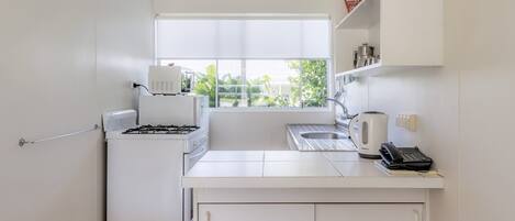 Une cuisine compacte avec des meubles blancs, une cuisinière à gaz, une bouilloire et une machine à café.