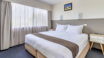 A hotel room with a large bed, a bedside table, a nightstand, and a window with curtains.