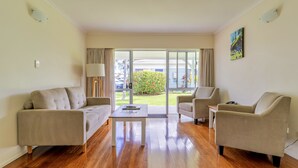 A modern living room with a sofa, armchairs, a coffee table, and a view of a garden through large sliding doors. - Aloha Apartments (Norfolk Island)