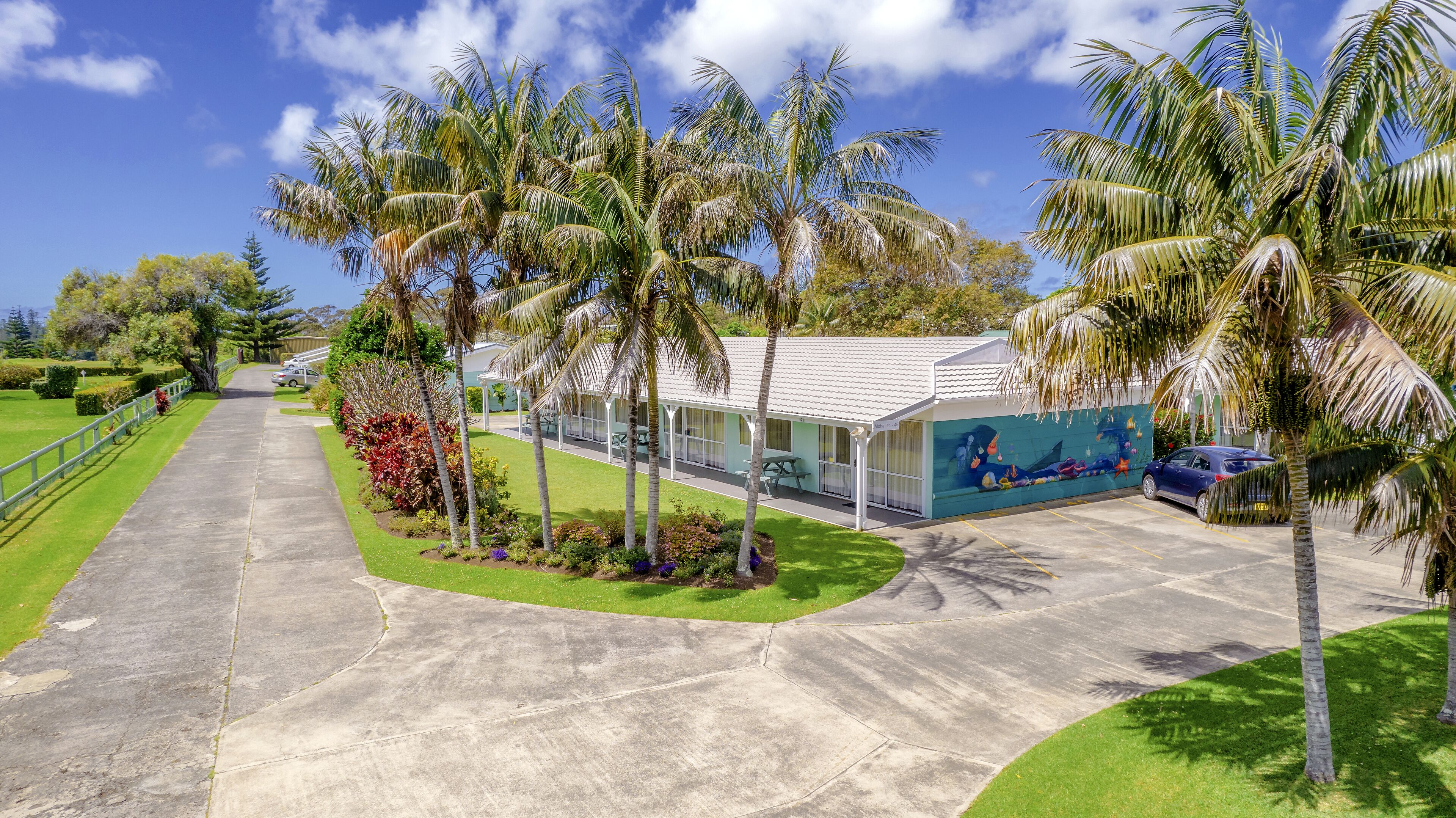 A hotel with a paved driveway, palm trees, and a mural on the building.