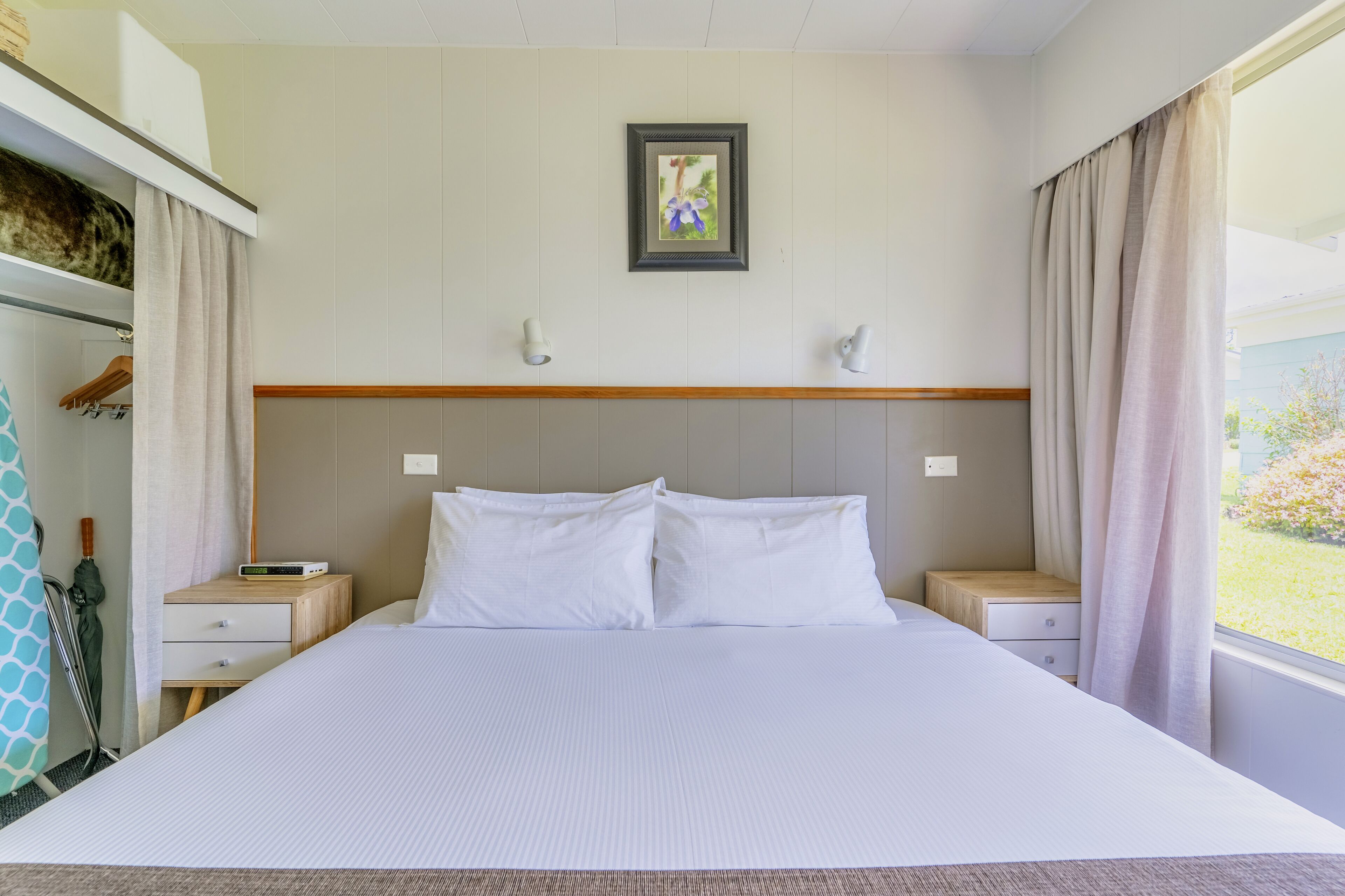 Una habitación de hotel con una cama grande, dos mesitas de noche, un armario y una ventana con cortinas.