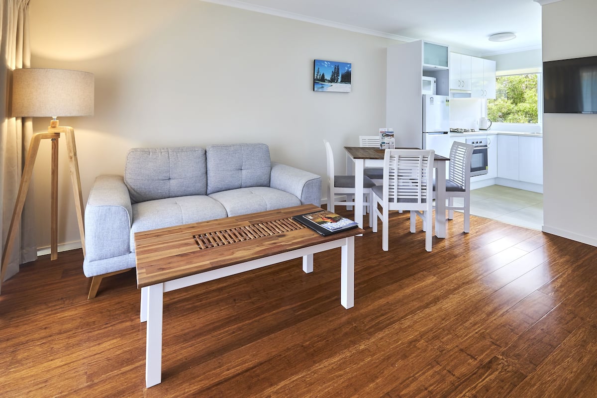 A modern living room with a sofa, a wooden coffee table, and a dining area with chairs.