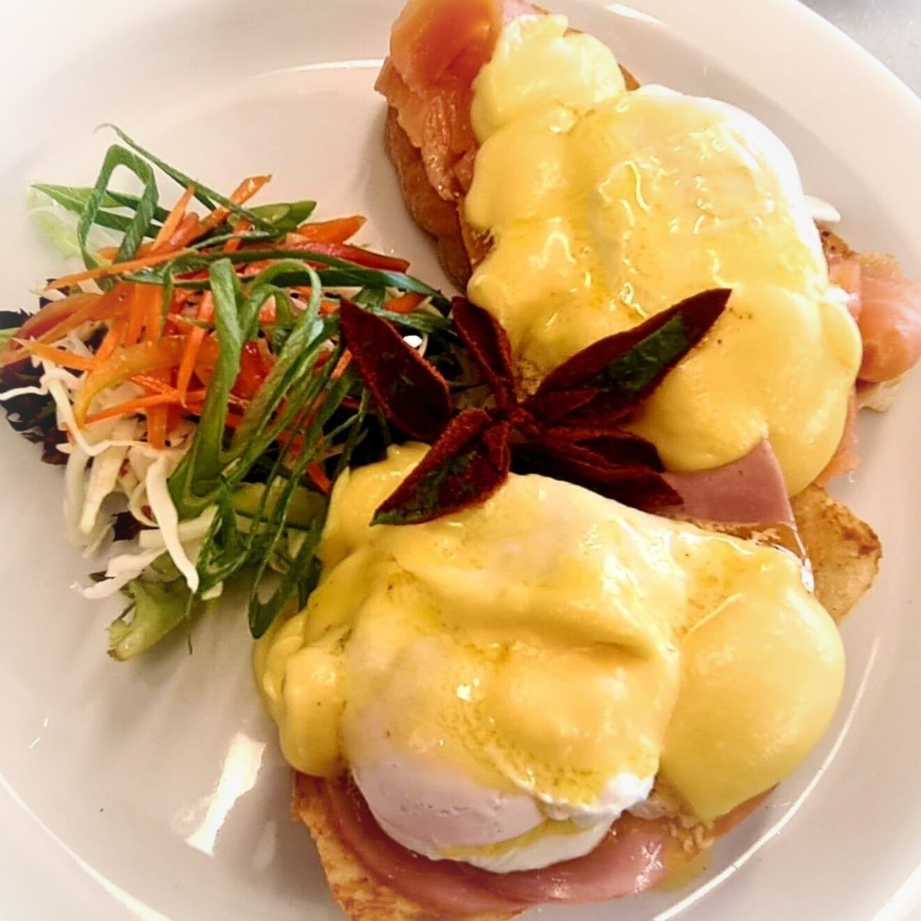 A breakfast plate with eggs Benedict, smoked salmon, and a side salad.
