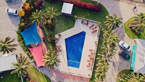 An aerial view of a residential property with a swimming pool, palm trees, and a patio area with lounge chairs. - Aloha Apartments (Norfolk Island)