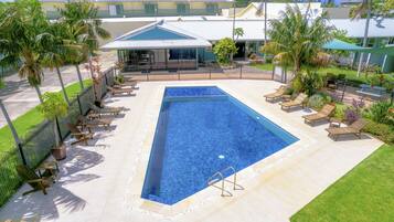 A rectangular pool with a tiled edge, surrounded by lounge chairs and palm trees.