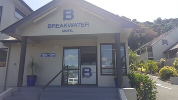 Motel Breakwater con mostrador de recepción, un gran logo en forma de 'B' y un cartel de recepción que indica los horarios de atención.