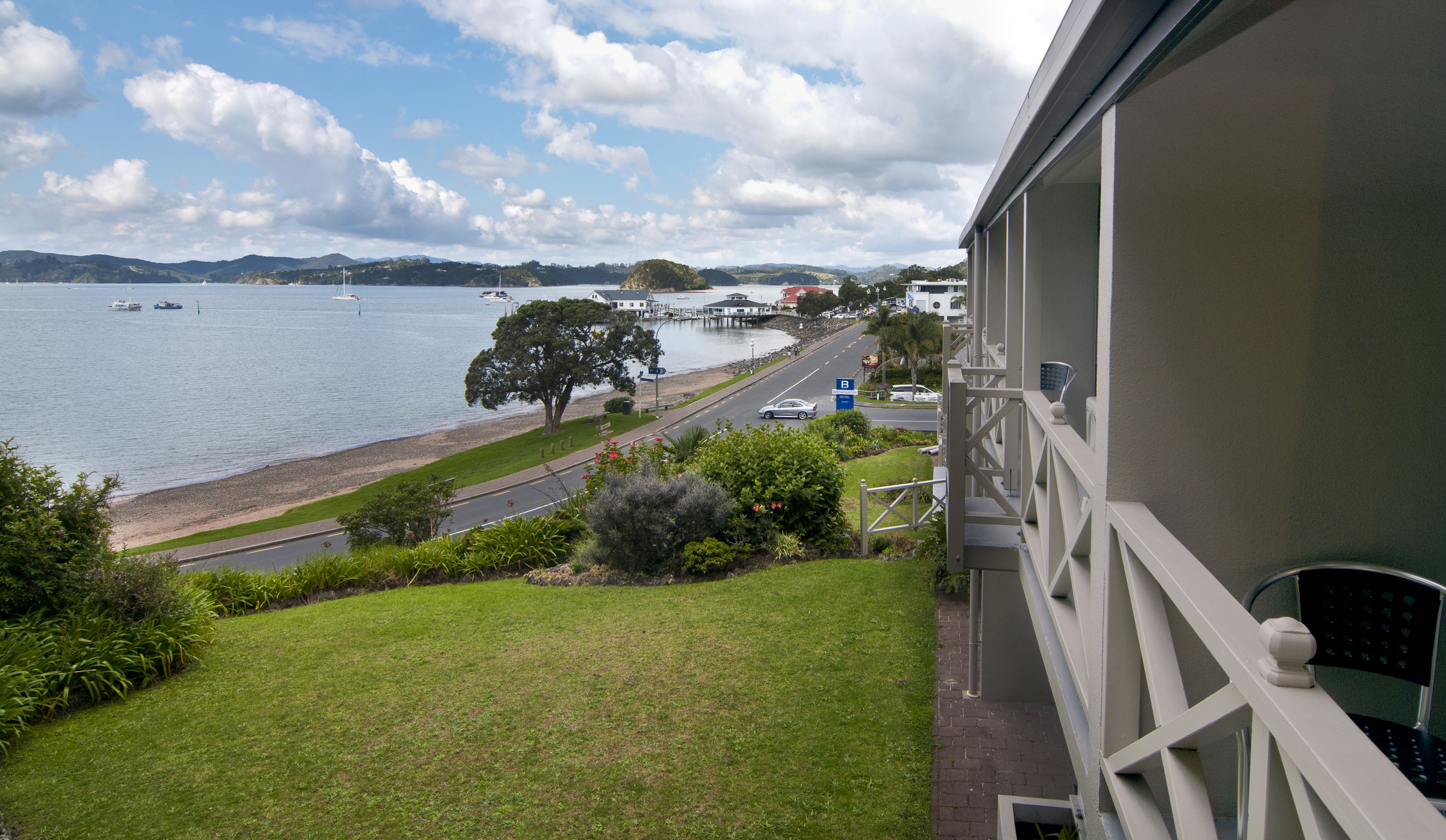 A balcony with a view of a lake, a road, and a parking area.
