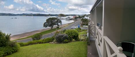 A balcony with a view of a lake, a road, and a parking area.