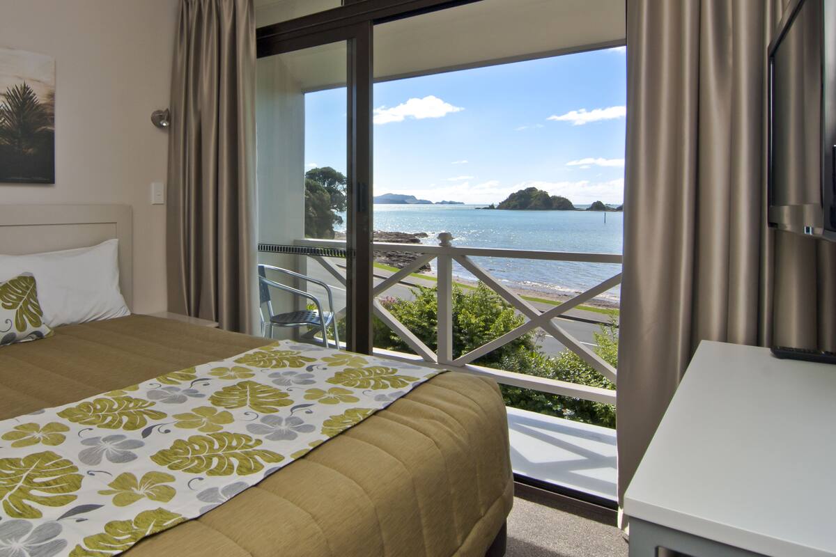 Quarto de hotel com uma cama, um quadro na parede e uma varanda com vista para o mar.