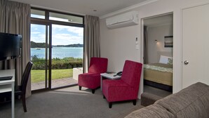 A hotel room with a TV, two red chairs, a sofa, a bed, and a large window with a view of the sea. - Breakwater Motel (Paihia)