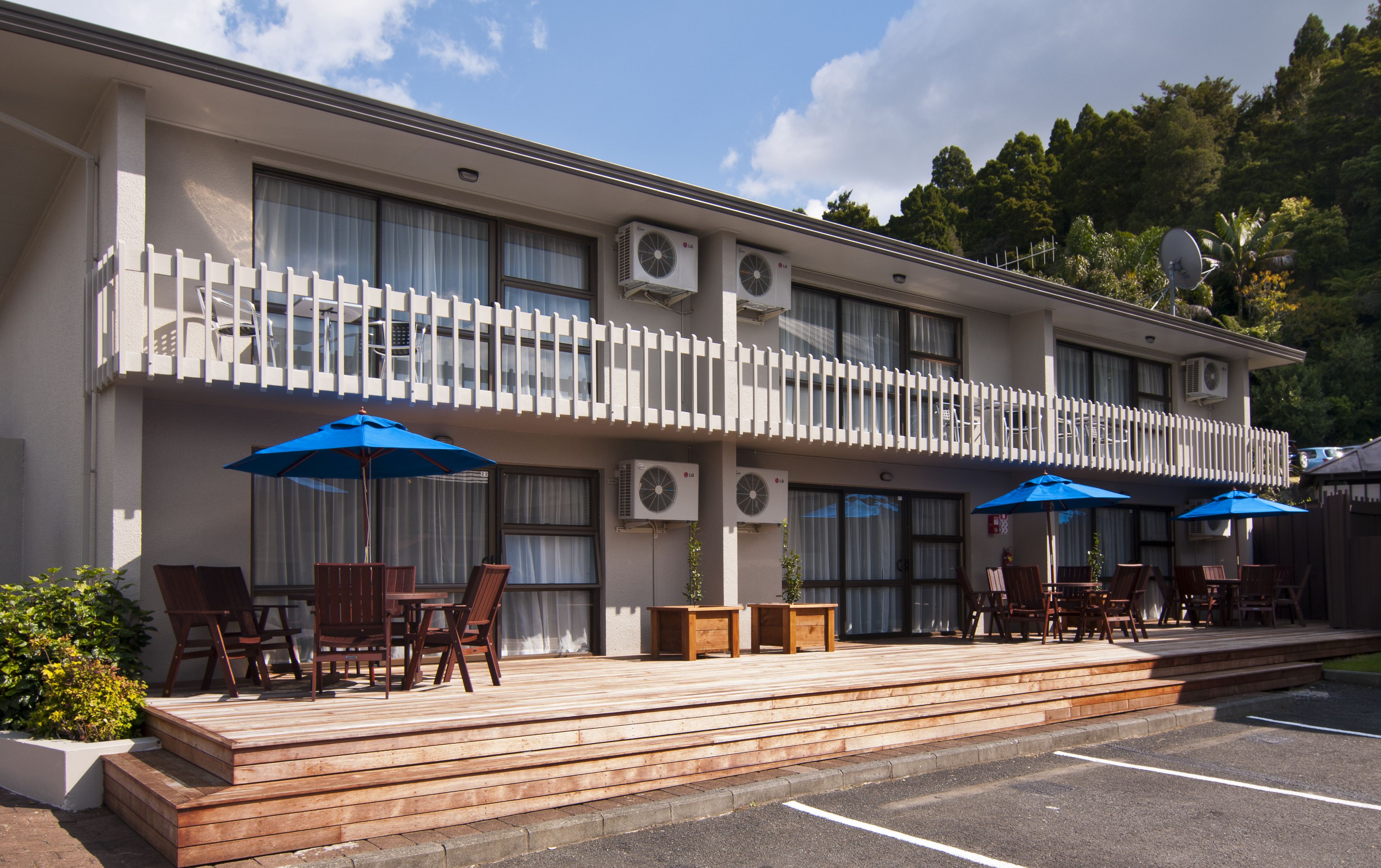 Hotel com um deck de madeira, área de estar externa com guarda-sóis e aparelhos de ar condicionado na fachada.