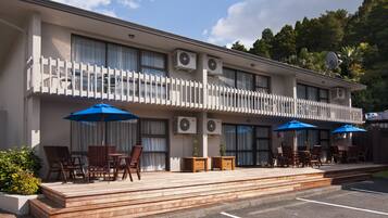 Hotel com um deck de madeira, área de estar externa com guarda-sóis e aparelhos de ar condicionado na fachada.