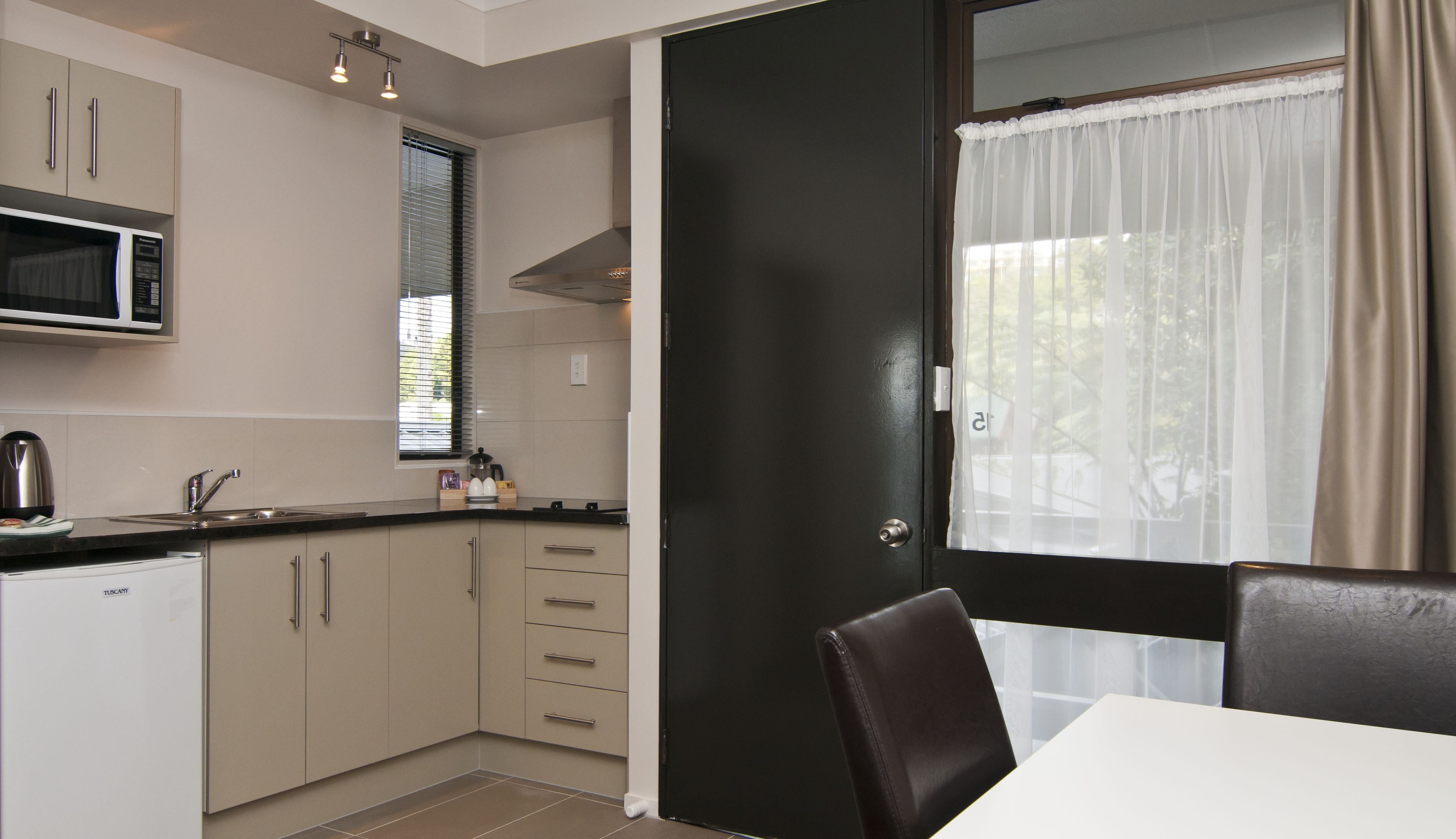 A modern kitchen with a microwave, sink, and cabinets, a dining area with a table and chairs, and a door leading to a balcony with a view.