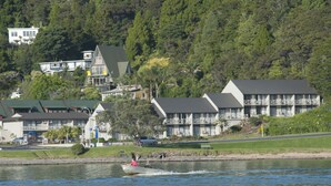 A lakeside view with a row of houses, including a large building with a balcony and a smaller building with a green roof. - Breakwater Motel (Paihia)