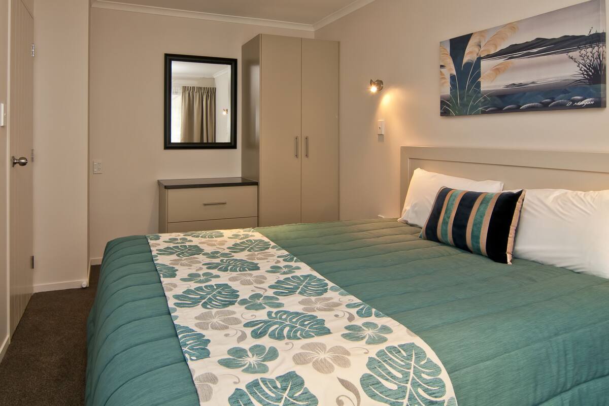 Quarto com cama, mesa de cabeceira, cômoda, espelho e um quadro na parede.