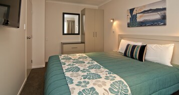 A bedroom with a bed, a nightstand, a dresser, a mirror, and a painting on the wall.