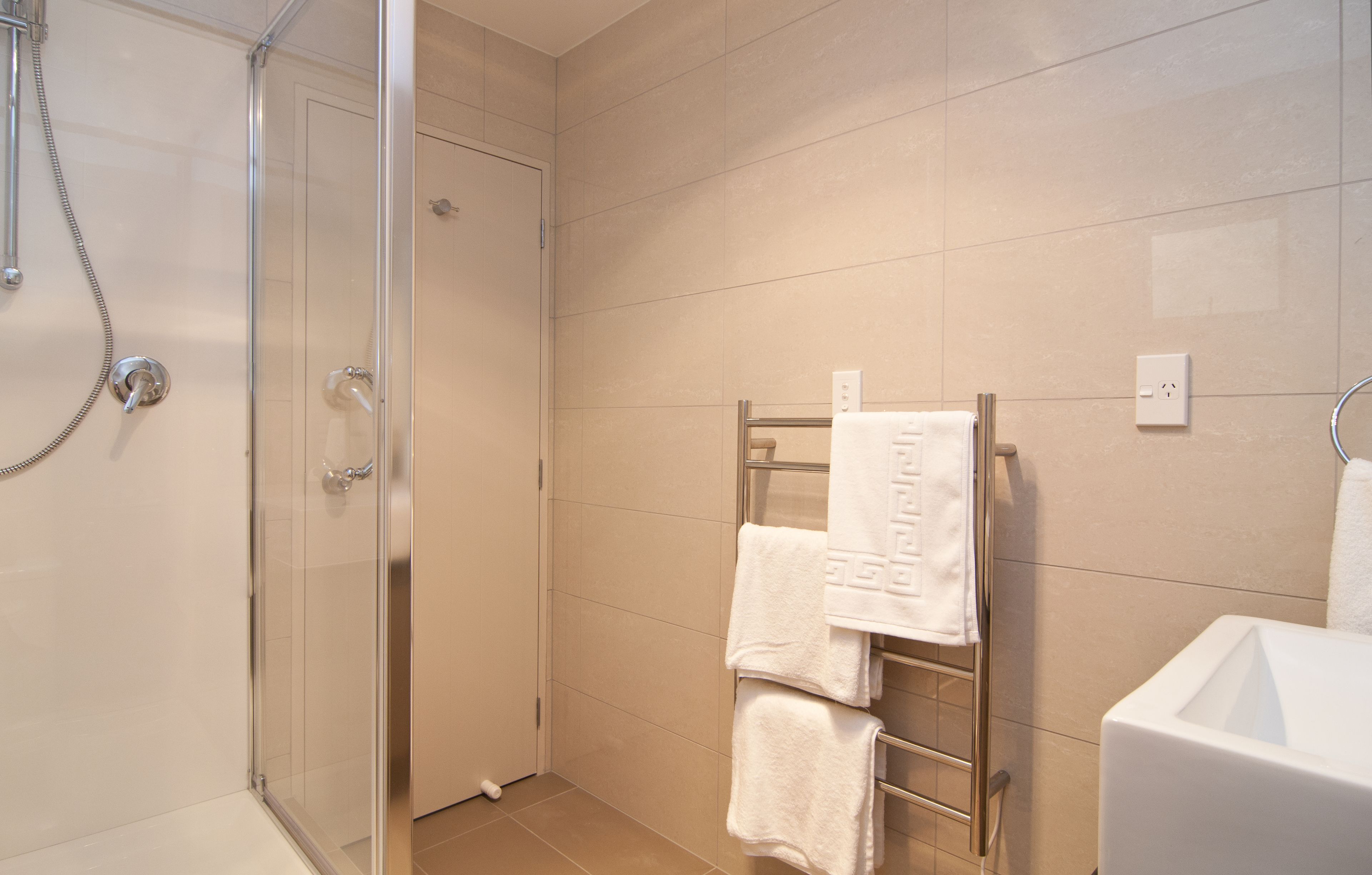 A modern bathroom with a glass shower enclosure, a white sink, and a towel rack with multiple towels.