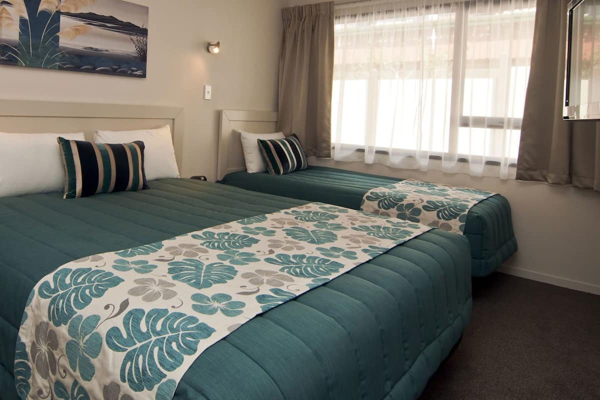 Quarto de hotel com duas camas, uma mesinha de cabeceira, um quadro na parede e uma janela com cortinas.