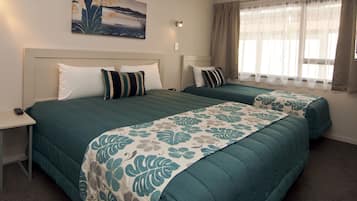 A hotel room with two beds, a nightstand, a painting on the wall, and a window with curtains.