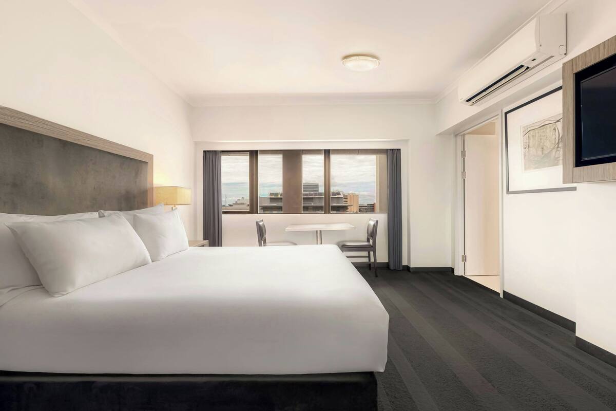 Habitación de hotel con una cama grande, un escritorio, una silla y una ventana con vistas a la ciudad.