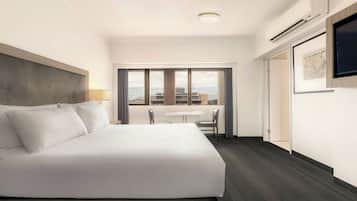Habitación de hotel con una cama grande, un escritorio, una silla y una ventana con vistas a la ciudad.