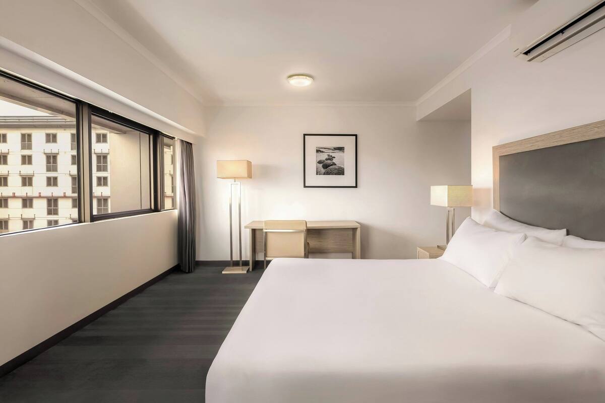 Habitación de hotel con una cama grande, un escritorio, una silla, una lámpara y un cuadro en la pared.