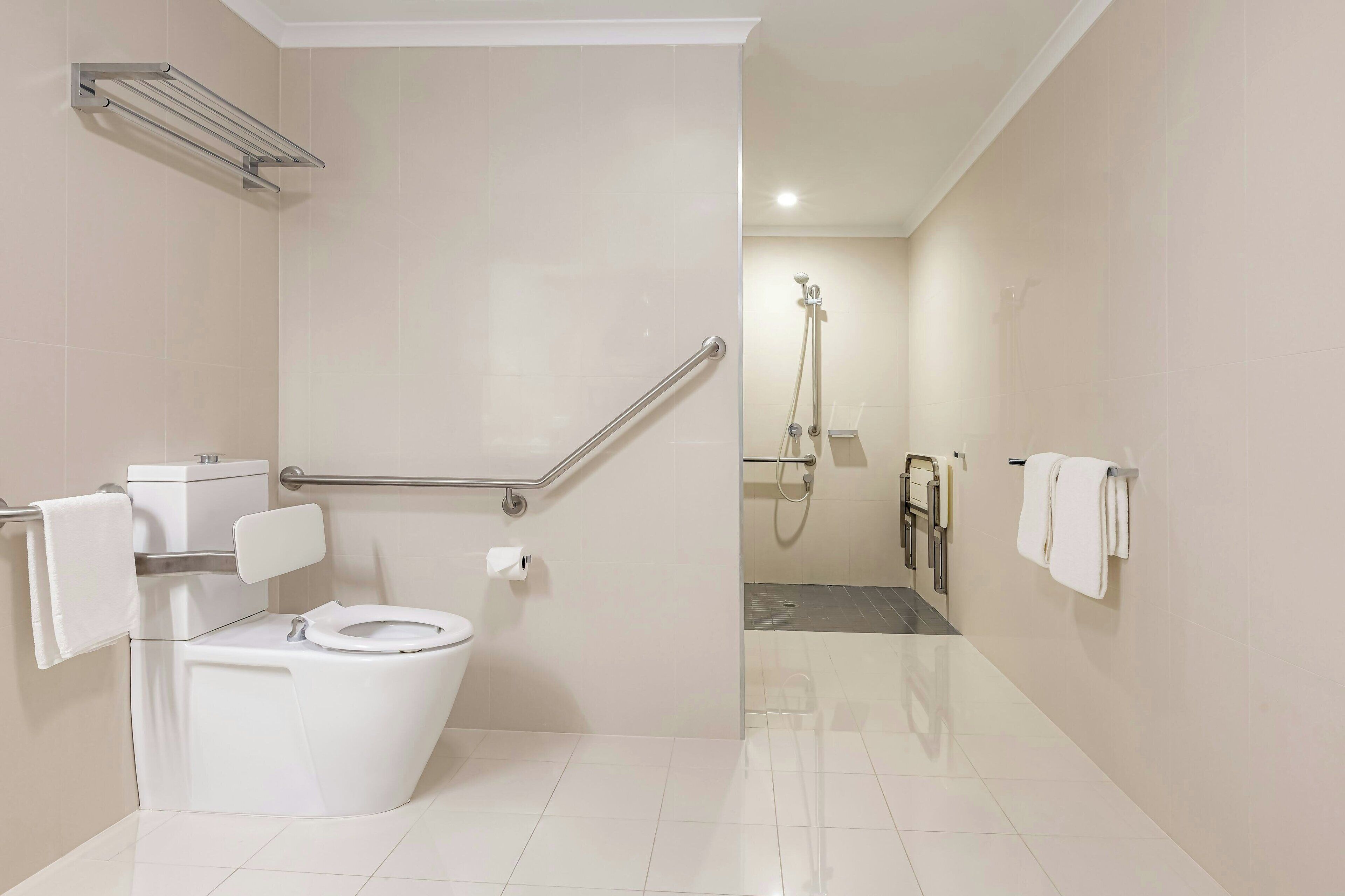 A modern bathroom with a white toilet, grab bars, a shower area, and a towel rack.