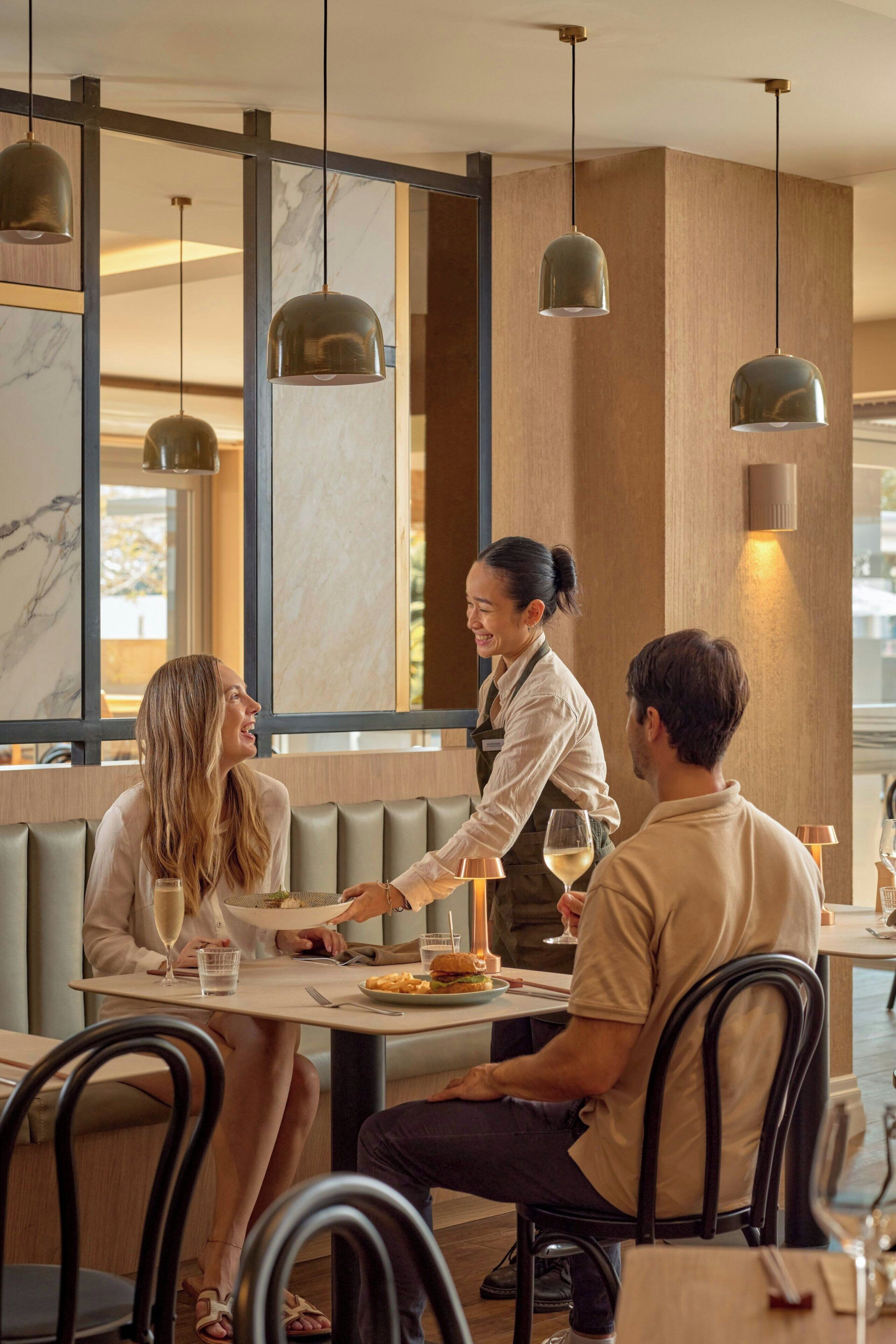Interior de restaurante com design moderno, apresentando paredes de mármore, iluminação pendente e ambiente descontraído para refeições.