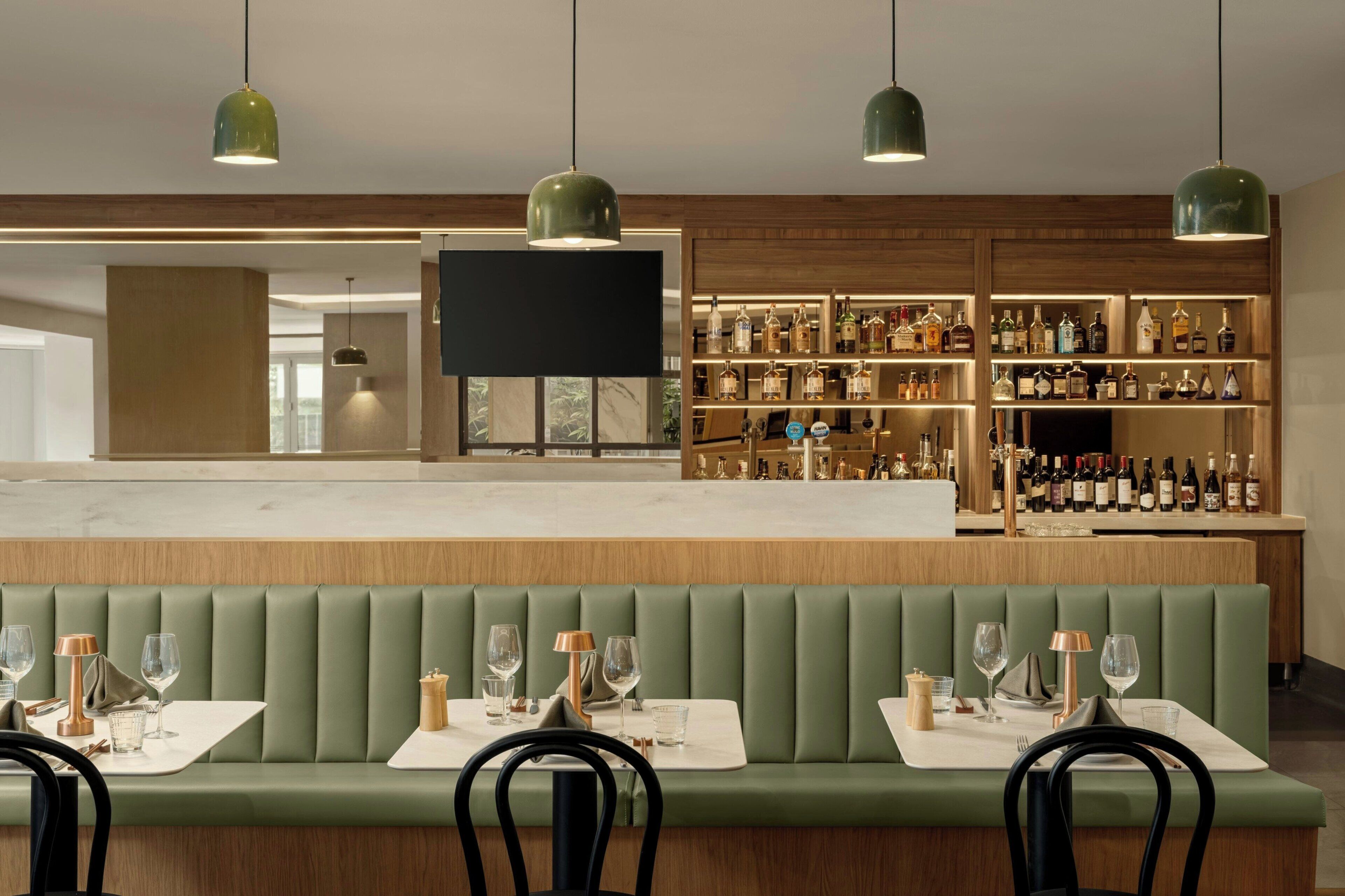 A bar area with a long counter, multiple shelves of bottles, and a seating area with tables and chairs.