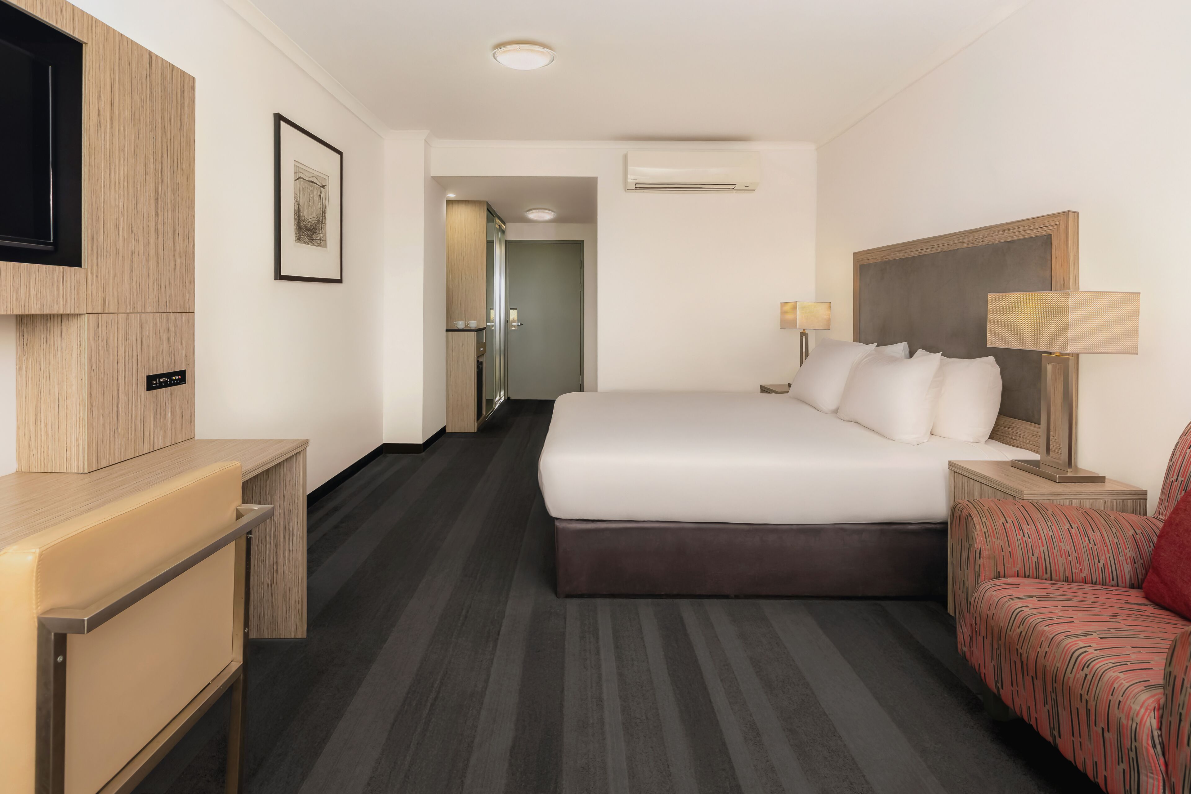 Een hotelkamer met een bed, een bureau, een stoel, een televisie, een deur en een airconditioning.