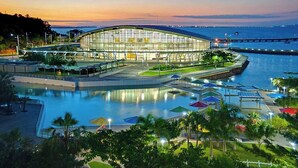A modern building with a large glass facade, a pool area with umbrellas, and a waterfront view. - Courtyard By Marriott Darwin (Darwin)