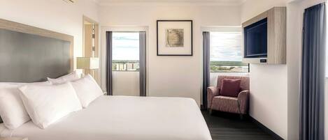 Habitación de hotel con una cama grande, un televisor montado en la pared, una silla y una ventana con vistas a la ciudad.