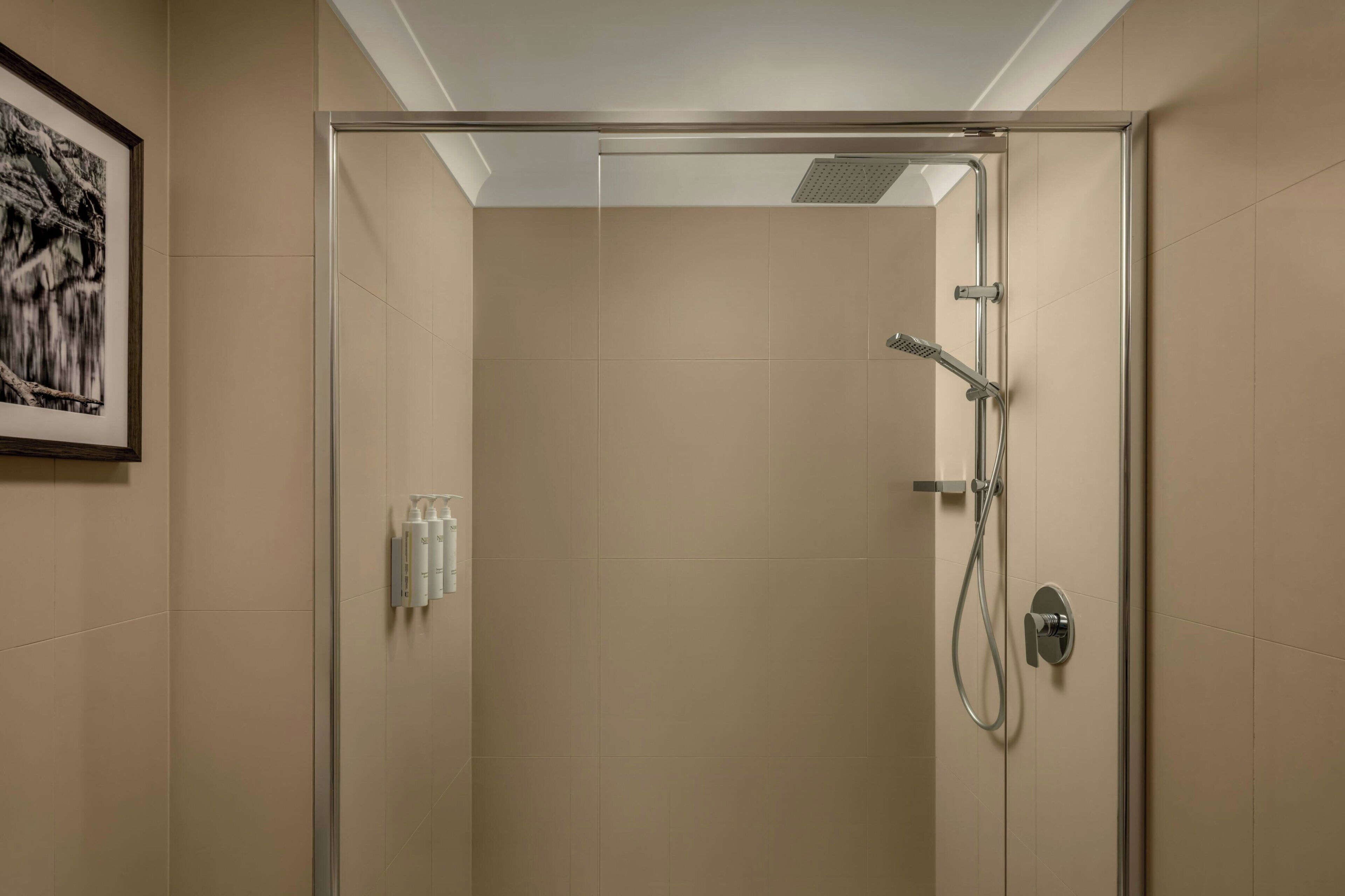 A modern shower room with a glass door, a handheld showerhead, and a wall-mounted control.