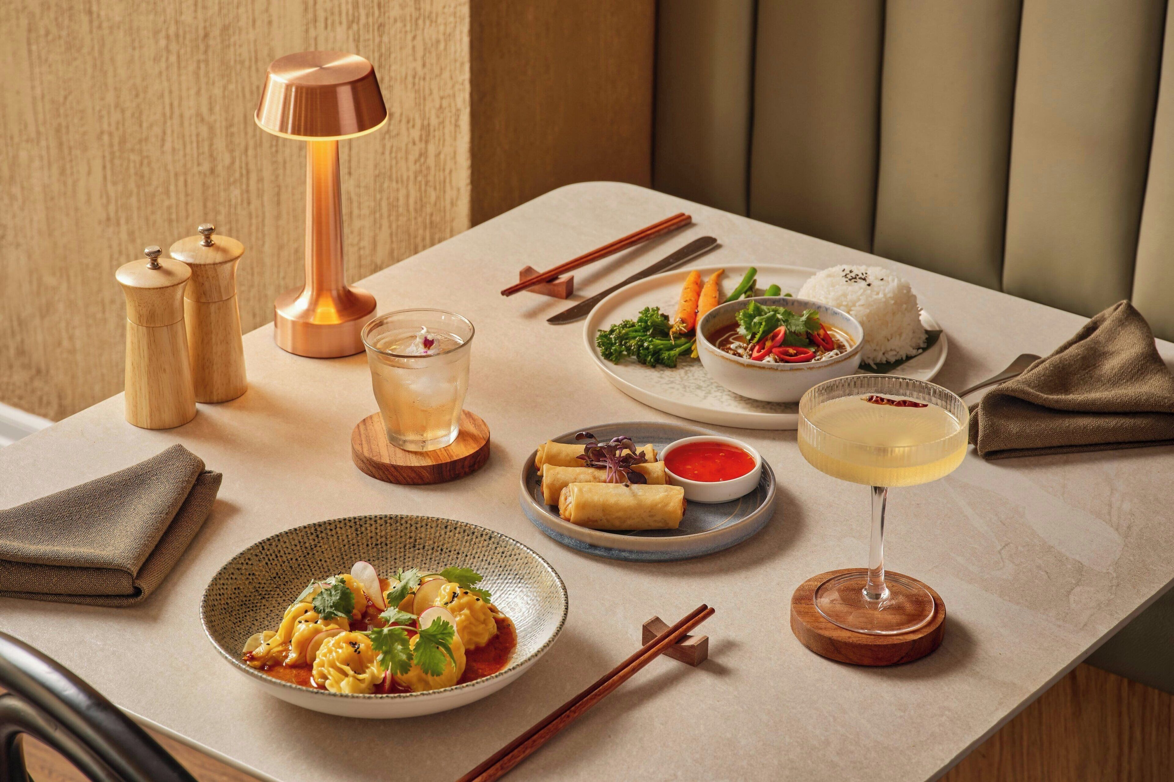A dining table with various dishes, a glass of drink, chopsticks, and a lamp.