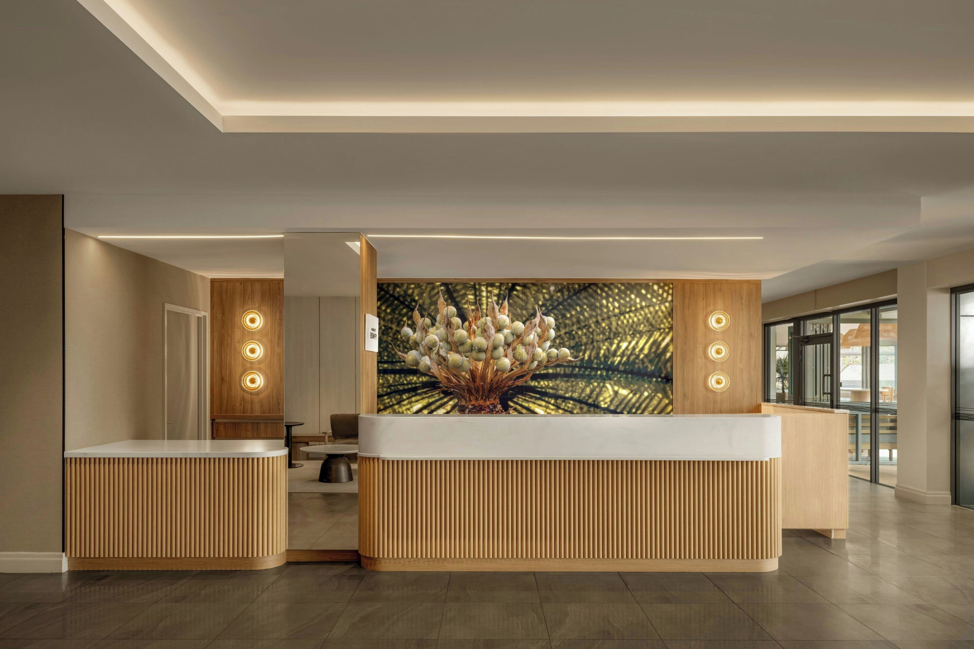 A reception area with a wooden reception desk, a large wall-mounted artwork, and a modern ceiling design.